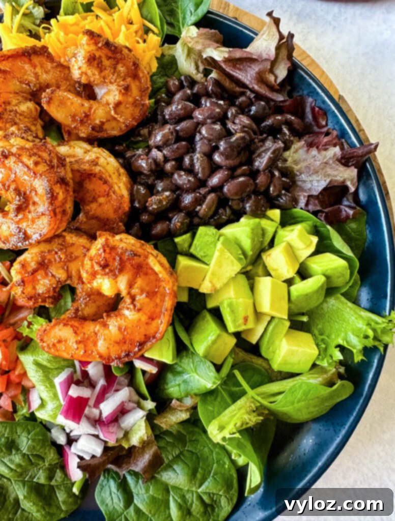 Zesty Shrimp Taco Bowl 11 A gourmet shrimp taco salad, generously topped with creamy avocado, sweet corn, black beans, savory onions, and a vibrant salsa, beautifully arranged on a blue plate.