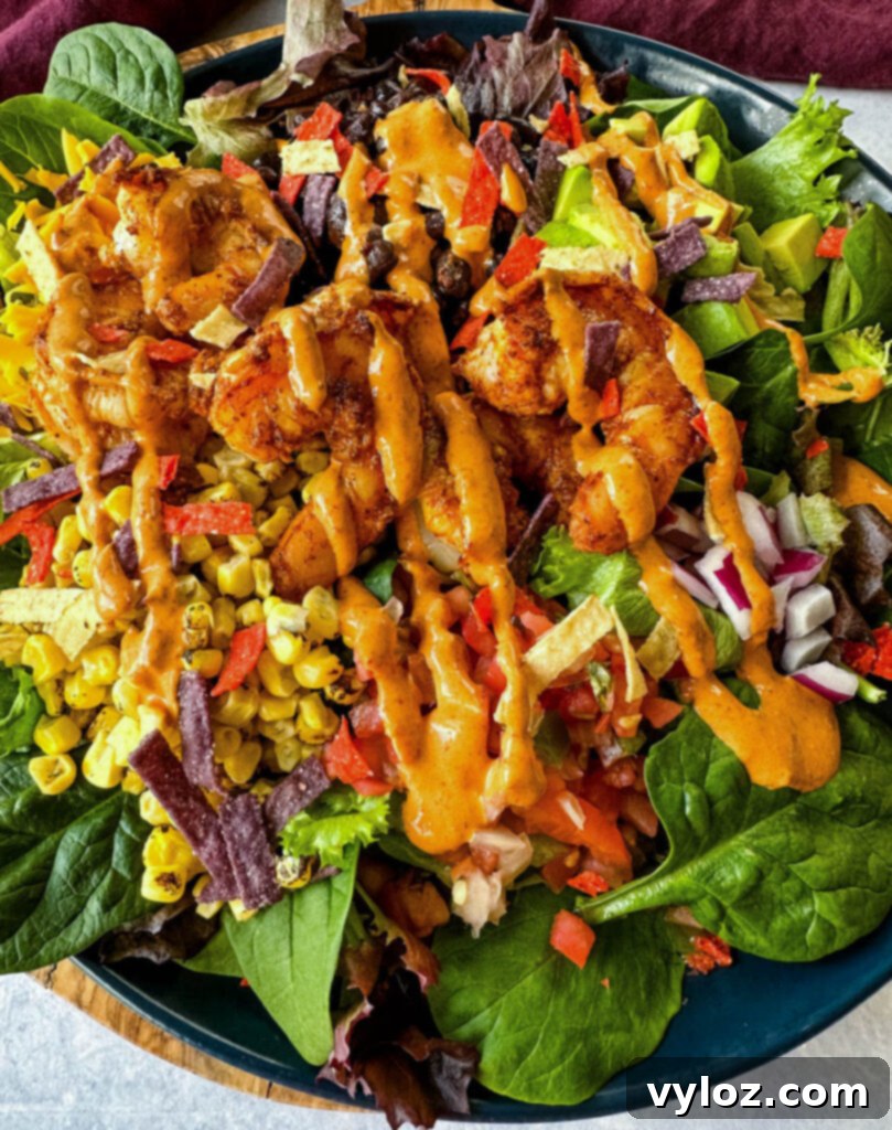 Zesty Shrimp Taco Bowl 12 A beautifully presented shrimp taco salad, complete with vibrant avocado, sweet corn, black beans, red onions, and salsa, all resting on a blue plate with a creamy Chipotle ranch dressing on the side.