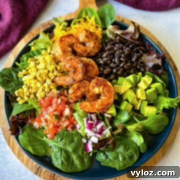 Zesty Shrimp Taco Bowl 13 A delicious shrimp taco salad featuring avocado, corn, black beans, onions, and salsa, presented on a blue plate.