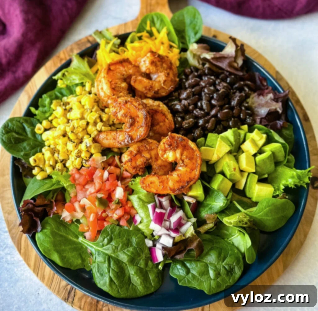 Zesty Shrimp Taco Bowl 9 A beautifully composed shrimp taco salad, featuring succulent shrimp, creamy avocado, sweet corn, savory black beans, and diced onions, all presented on a blue plate.