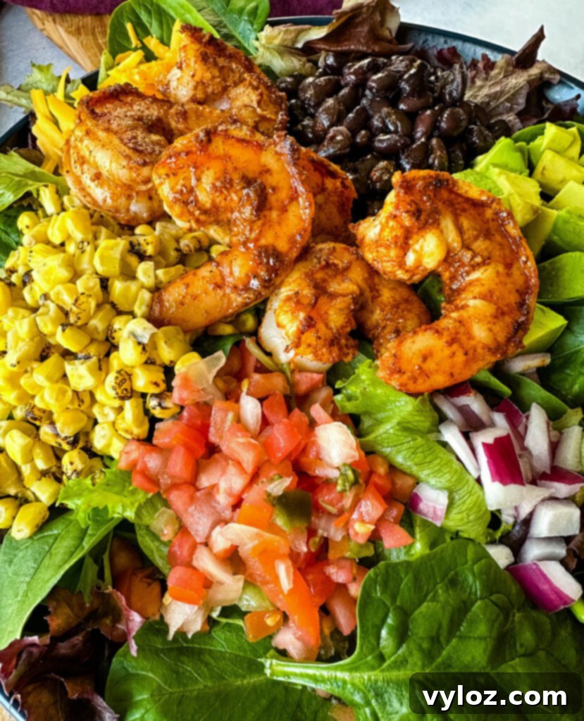 Zesty Shrimp Taco Bowl 10 A close-up shot of a delectable shrimp taco salad, adorned with creamy avocado, sweet corn, black beans, diced onions, and a vibrant salsa, served elegantly on a blue plate.