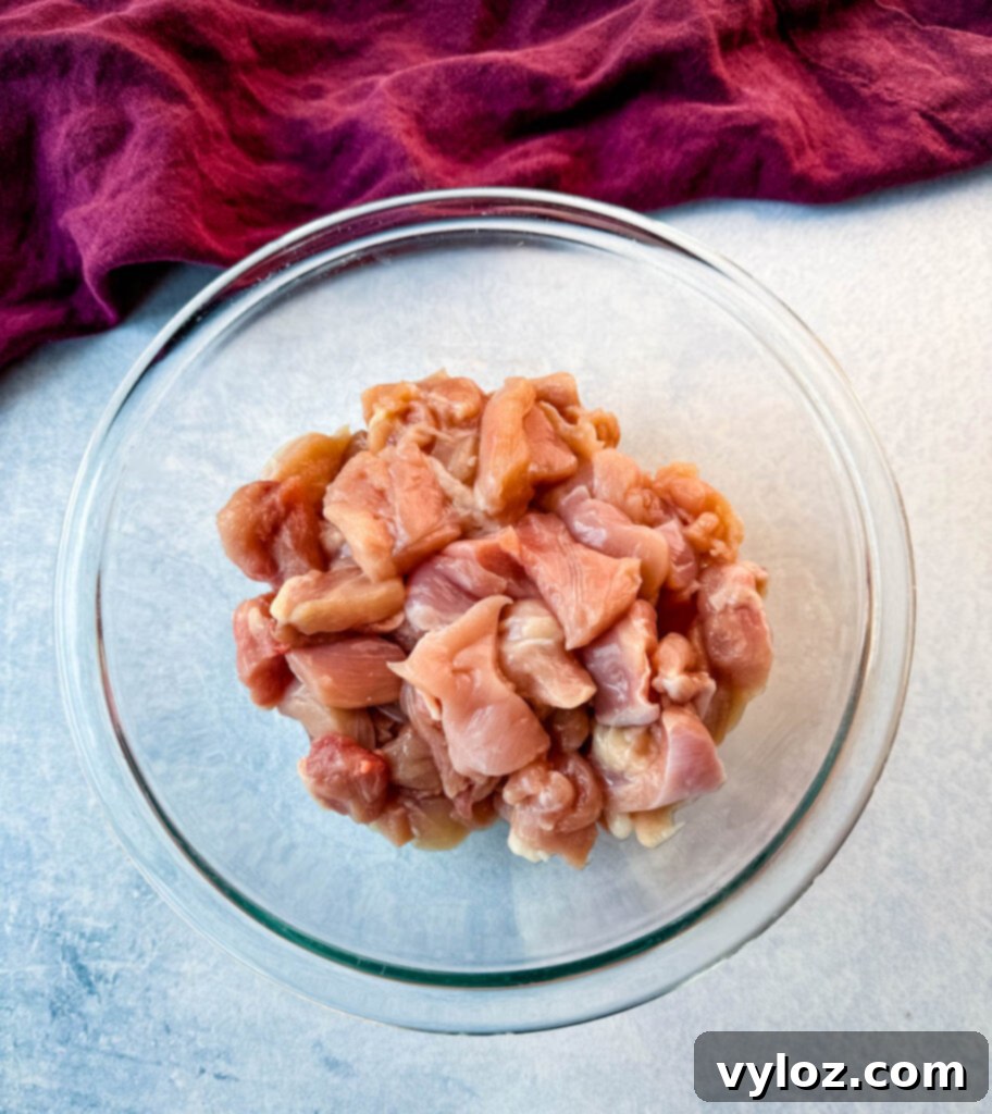Raw, diced chicken thighs in a clear glass bowl, showcasing the readiness of the protein for cooking.