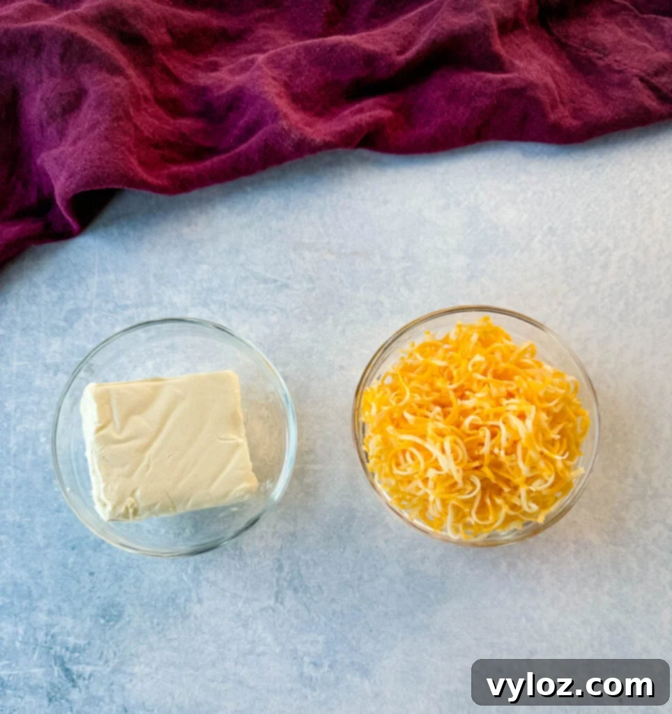 Two glass bowls, one filled with softened cream cheese and the other with grated Colby Jack cheese, ready to be incorporated into the recipe.