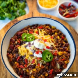 Taco Chili 11 beef taco chili in a white bowl with jalapenos, sour cream, shredded cheese, and tortilla chips