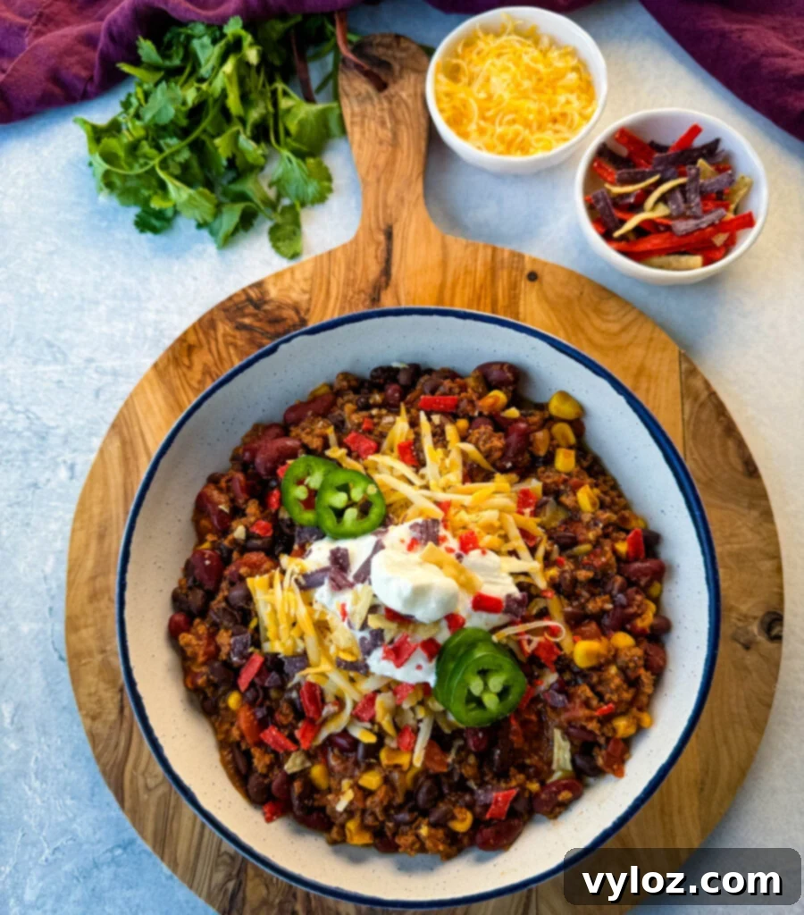 Taco Chili 8 beef taco chili in a white bowl with jalapenos, sour cream, shredded cheese, and tortilla chips
