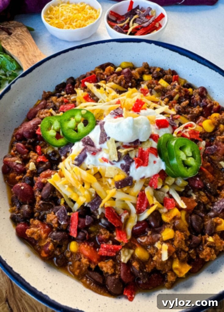 Taco Chili 10 beef taco chili in a white bowl with jalapenos, sour cream, shredded cheese, and tortilla chips