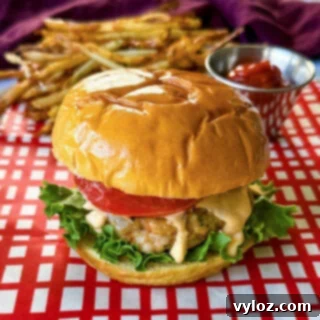 shrimp burger with lettuce, tomato, and spicy mayo on a plate with fries and ketchup