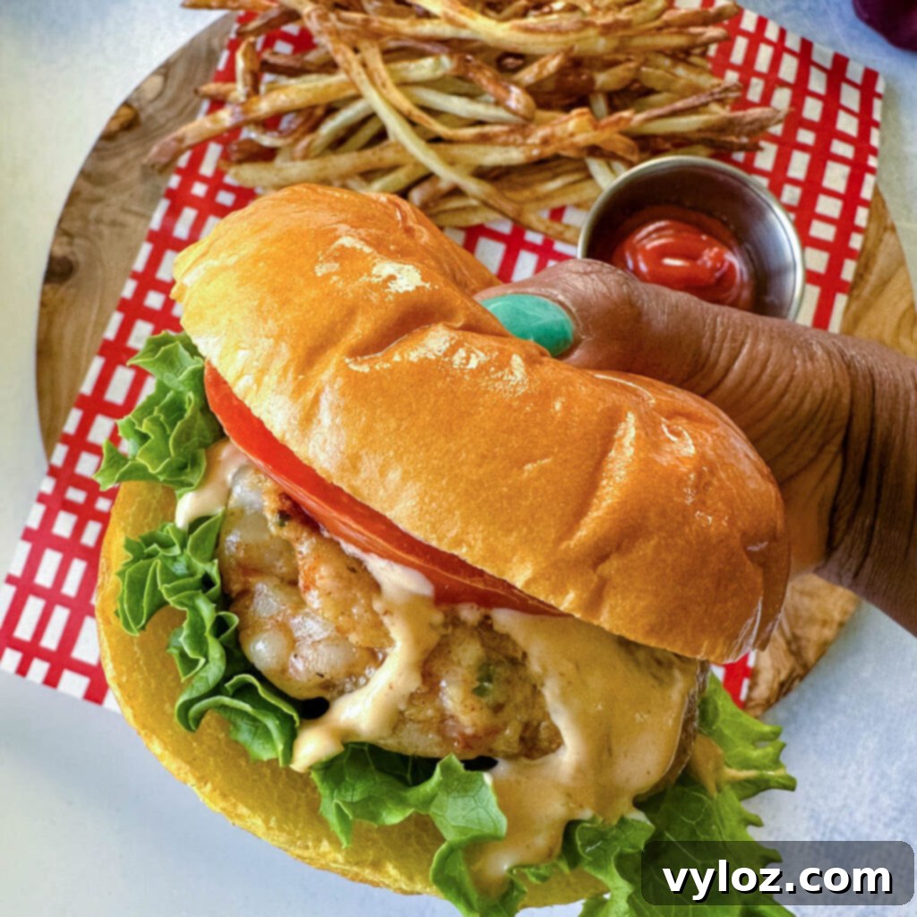 person holding shrimp burger with lettuce, tomato, and spicy mayo