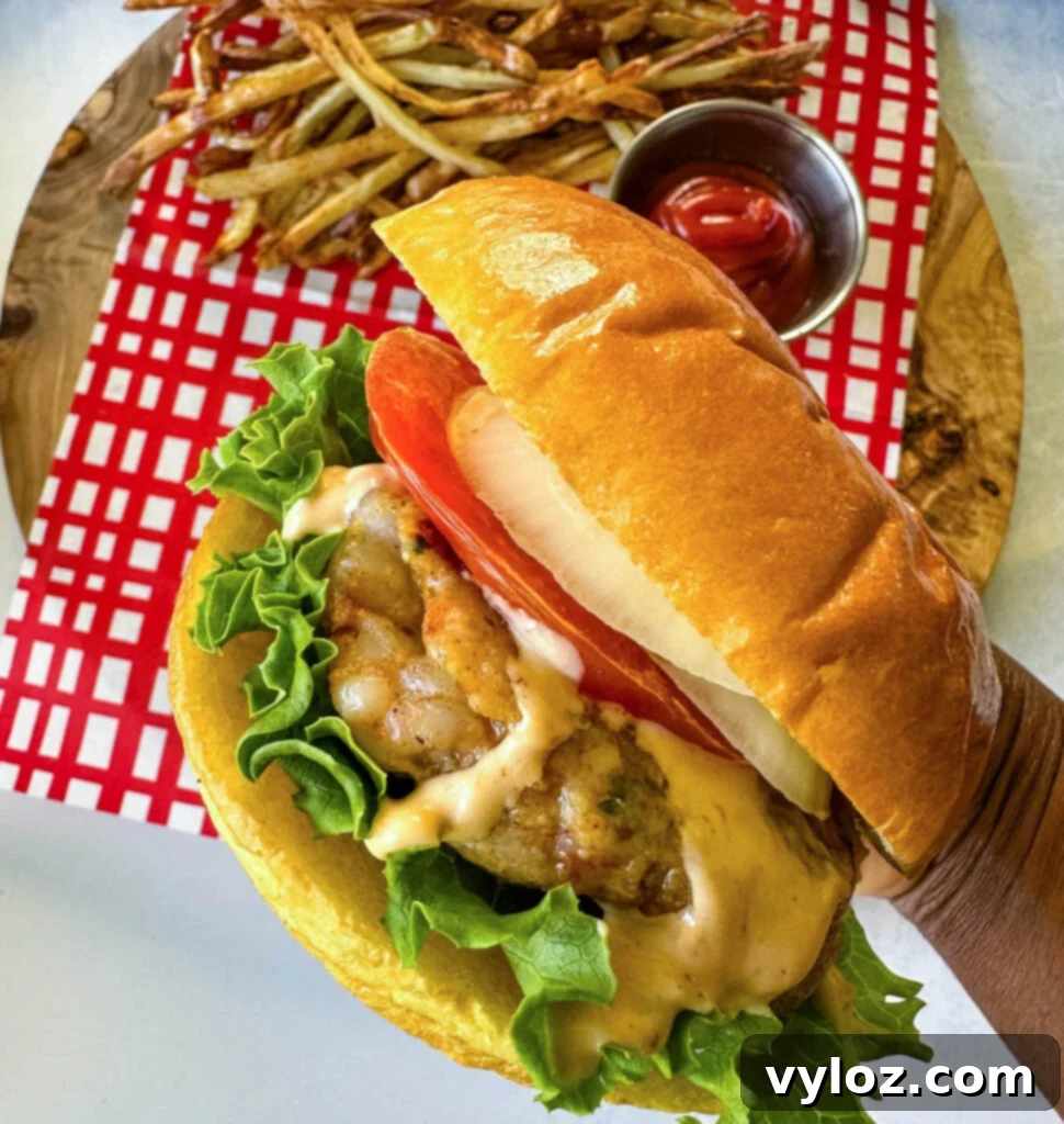 person holding shrimp burger with lettuce, tomato, and spicy mayo