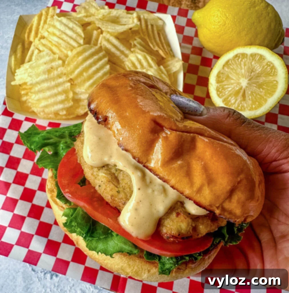 person holding crab cake sandwich with chips