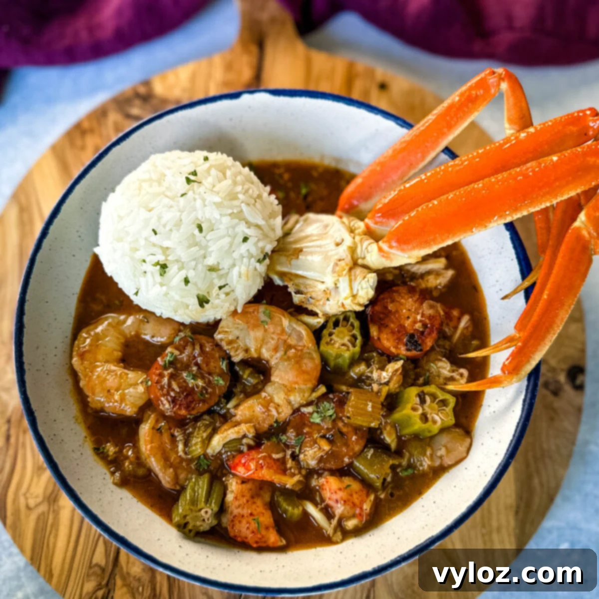 Rich Cajun seafood gumbo brimming with shrimp and crab meat, served with crab legs and a side of fluffy white rice in a pristine white bowl.