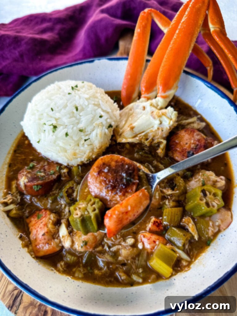 A wooden spoon lifting a spoonful of rich Cajun seafood gumbo, laden with plump shrimp, succulent crab meat, and a piece of crab leg, from a white bowl of gumbo with rice.