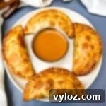 Golden Air Fryer Dessert Empanadas 18 Air Fryer Apple Cinnamon Dessert Empanadas on a white plate with caramel
