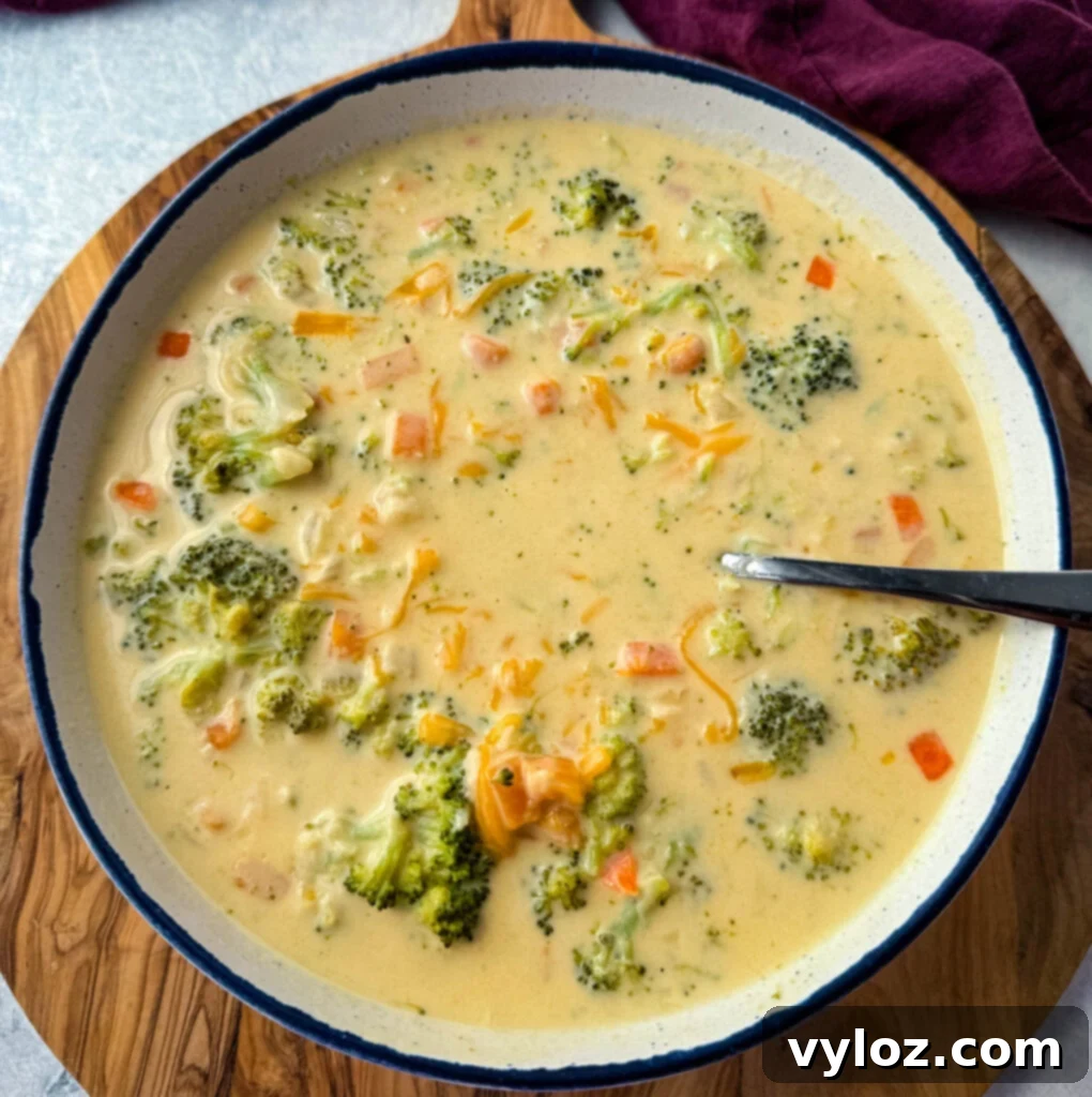 Velvety Broccoli Cheddar Soup 10 broccoli cheddar soup in a white bowl with a spoon and grated cheddar cheese