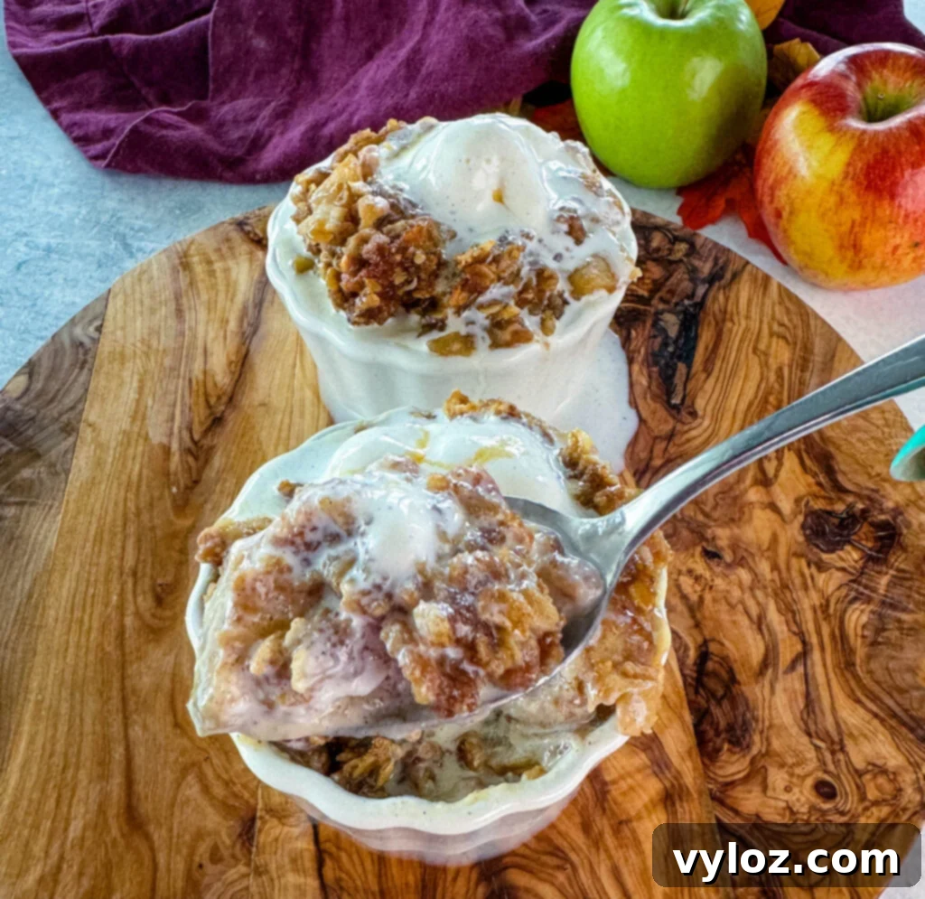 Effortless Crockpot Apple Crumble 12 a spoonful of slow cooker Crockpot apple crisp in a white bowl with a scoop of vanilla ice cream and caramel