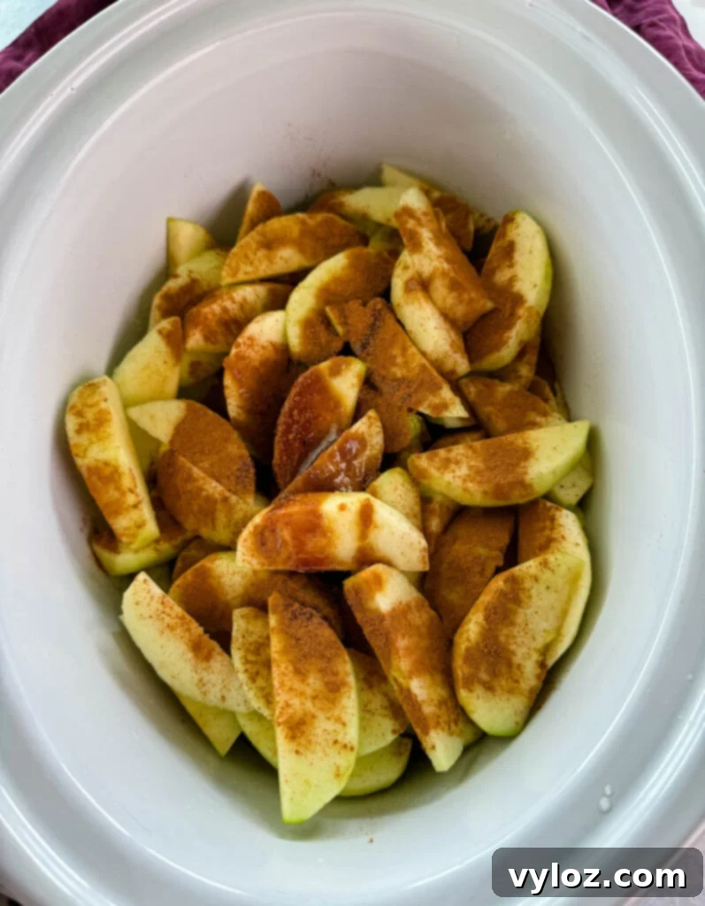 Effortless Crockpot Apple Crumble 4 sliced apples with cinnamon and sugar in a white Crockpot slow cooker