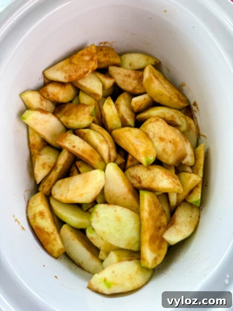 Effortless Crockpot Apple Crumble 5 sliced apples with cinnamon and sugar in a white Crockpot slow cooker