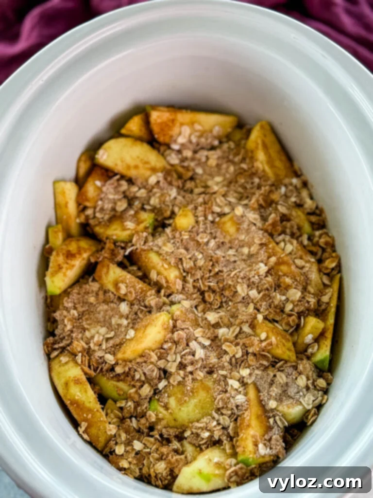 Effortless Crockpot Apple Crumble 7 sliced apples with cinnamon and sugar with a crumble topping in a white Crockpot slow cooker