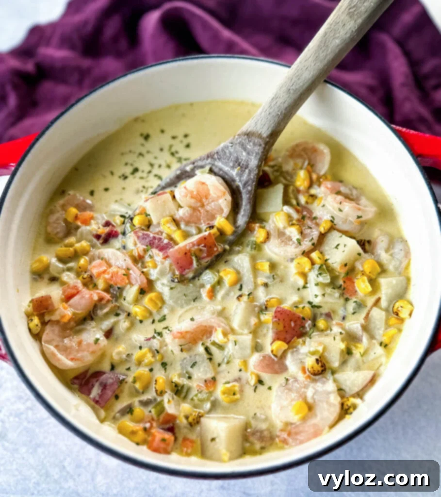 shrimp and corn chowder with bacon and potatoes with a wooden spoon in a Dutch oven
