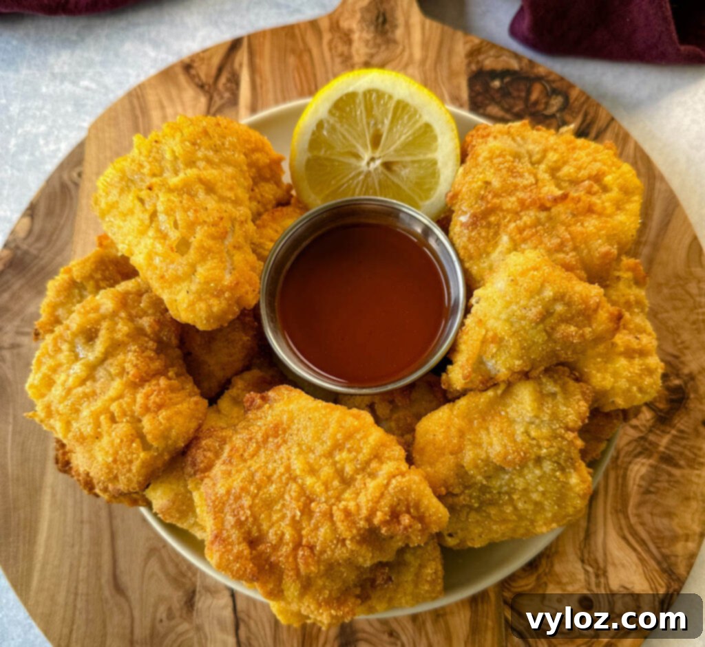 Simple Catfish Nuggets 2 breaded catfish nuggets on a plate with hot sauce and a fresh lemon