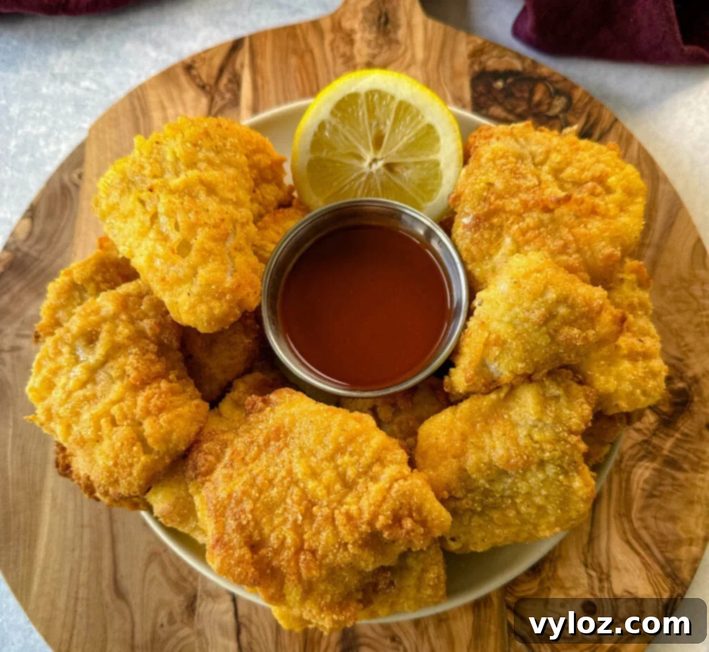 Crispy Fish Fry Mix 2 Crispy breaded catfish nuggets served on a plate with hot sauce and a fresh lemon wedge.