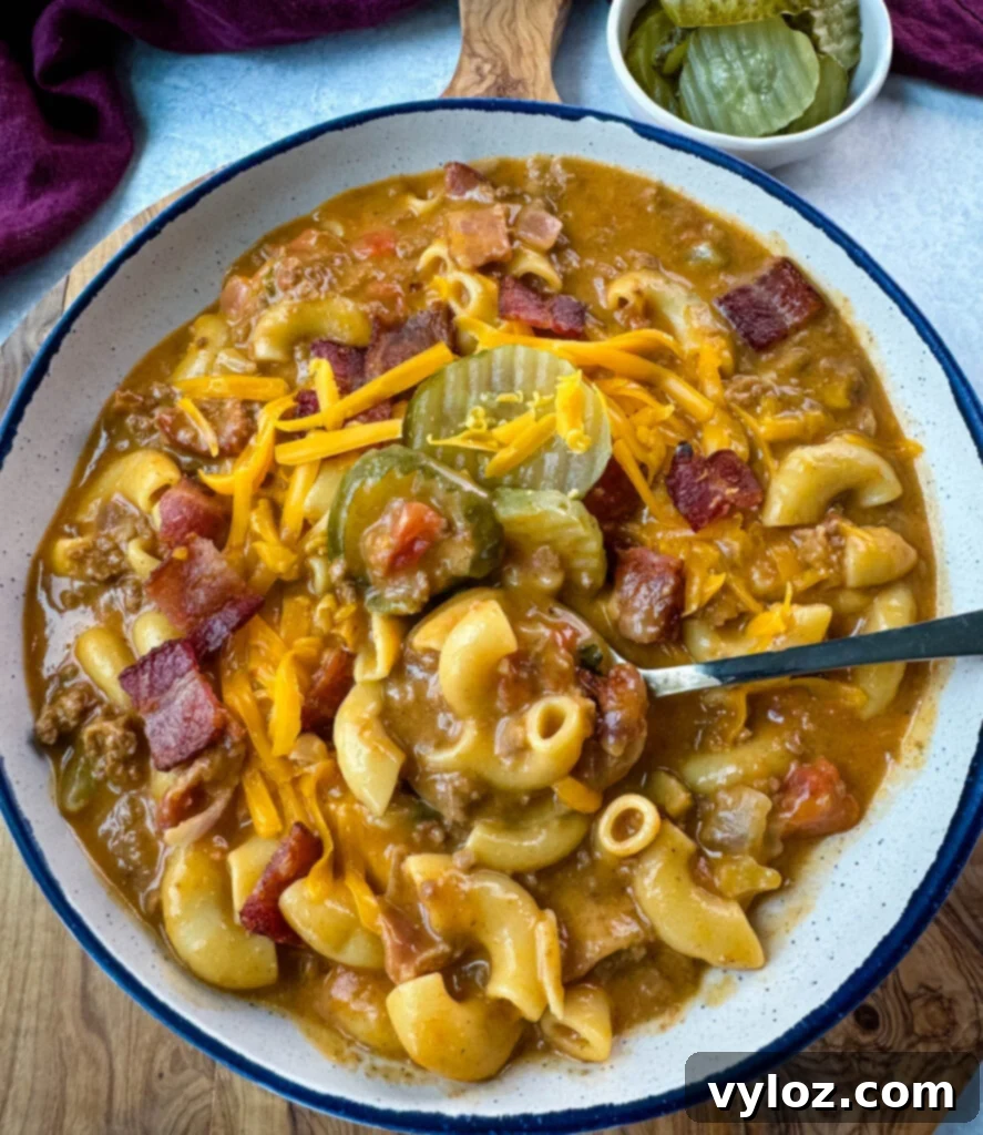Savory Bacon Cheeseburger Mac Soup 12 bacon cheeseburger soup with pickles and grated cheese in a white bowl