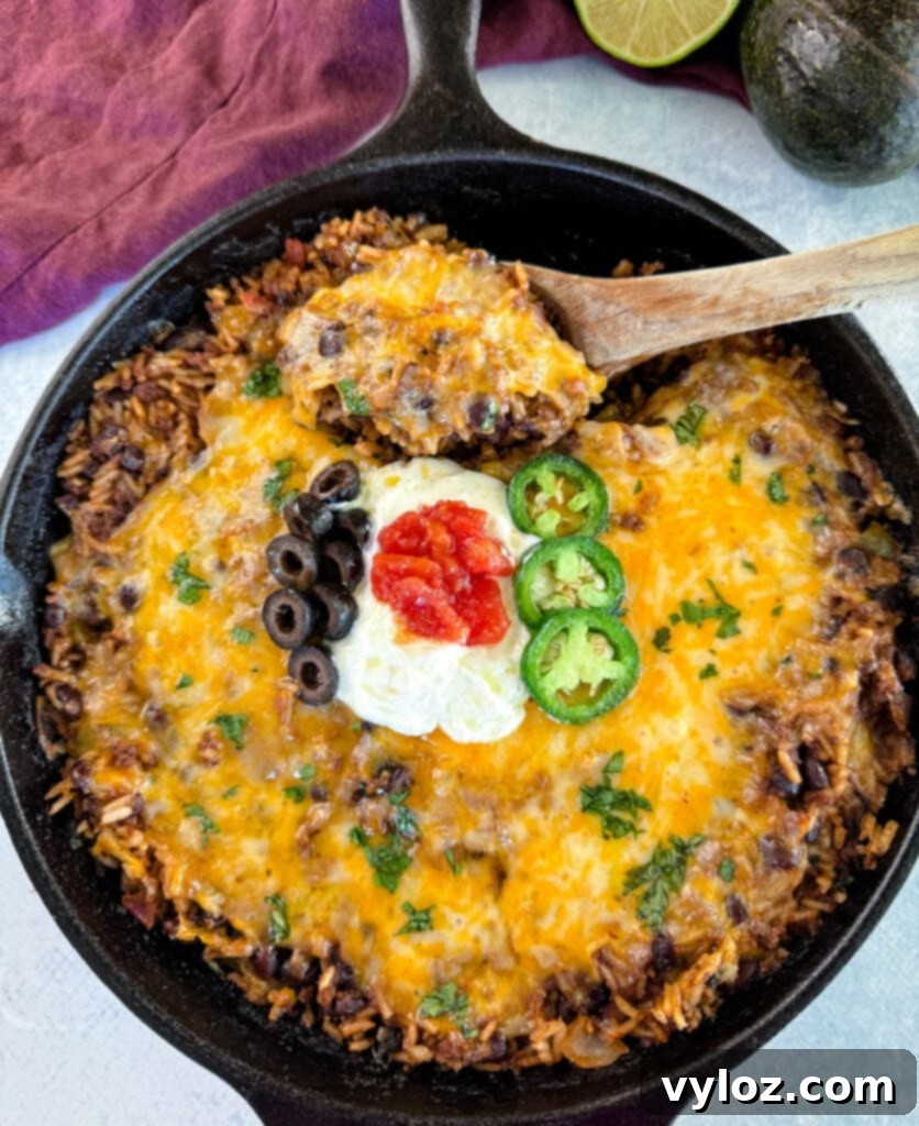 Mexican beef and rice taco skillet dish in a cast iron skillet with a wooden spoon and sour cream, tomatoes, and black olives