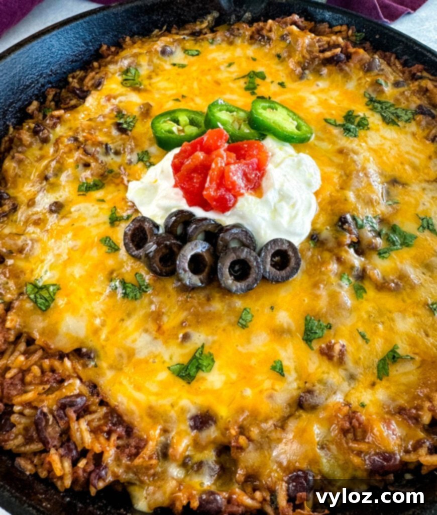 Mexican beef and rice taco skillet dish in a cast iron skillet with sour cream, tomatoes, and black olives