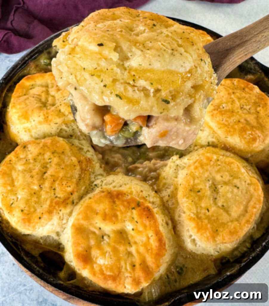A wooden spoonful of creamy chicken pot pie with fluffy biscuits in a cast iron skillet, ready to be served.