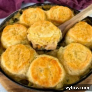 a wooden spoonful of chicken pot pie with biscuits in a cast iron skillet