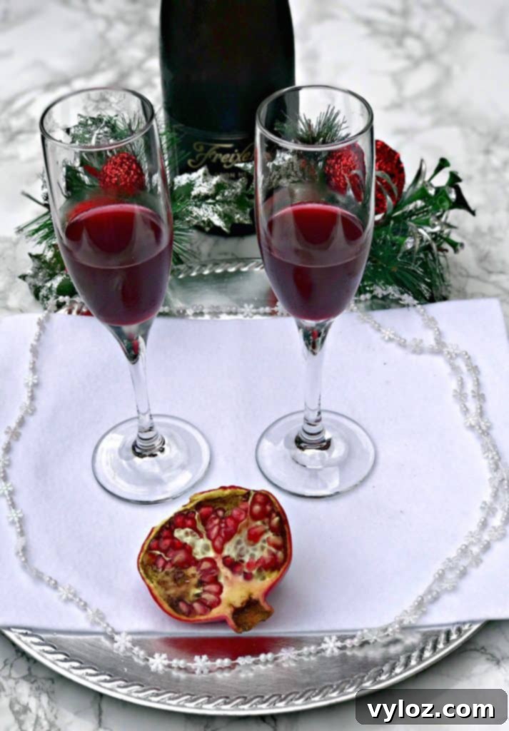 Ruby Red Holiday Fizz 4 Close-up of a single Pomegranate Holiday Mimosa, showcasing its vibrant red hue and delicate effervescence, surrounded by subtle holiday decor.