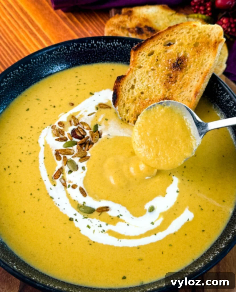 A spoonful of creamy butternut squash soup in a bowl, garnished with cream, nuts, and toasted bread