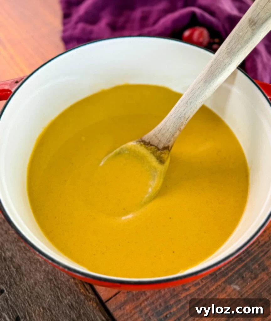 Creamy butternut squash soup in a Dutch oven with a wooden spoon