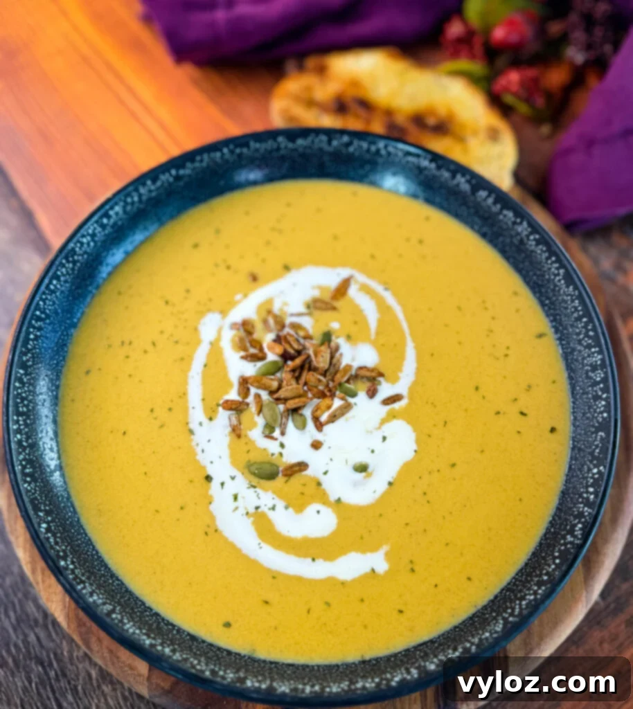 Creamy butternut squash soup in a bowl, garnished with cream, toasted nuts, and a slice of toasted bread on the side