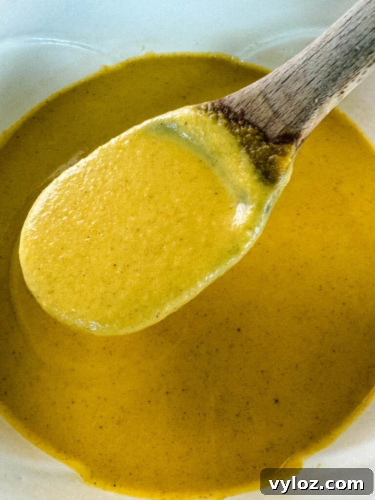 A wooden spoonful of creamy butternut squash soup, garnished with a swirl of cream and fresh herbs