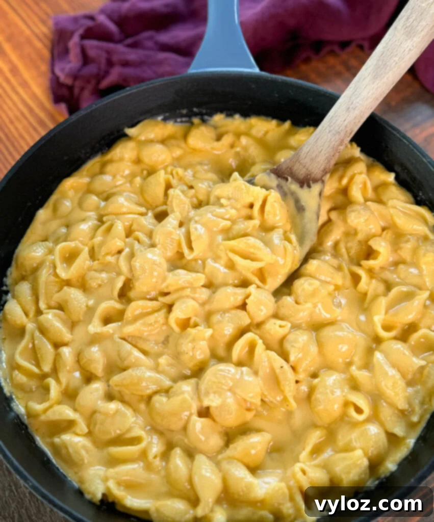 A wooden spoon scooping a generous portion of freshly made stovetop mac and cheese from a cast iron skillet, highlighting its creamy texture