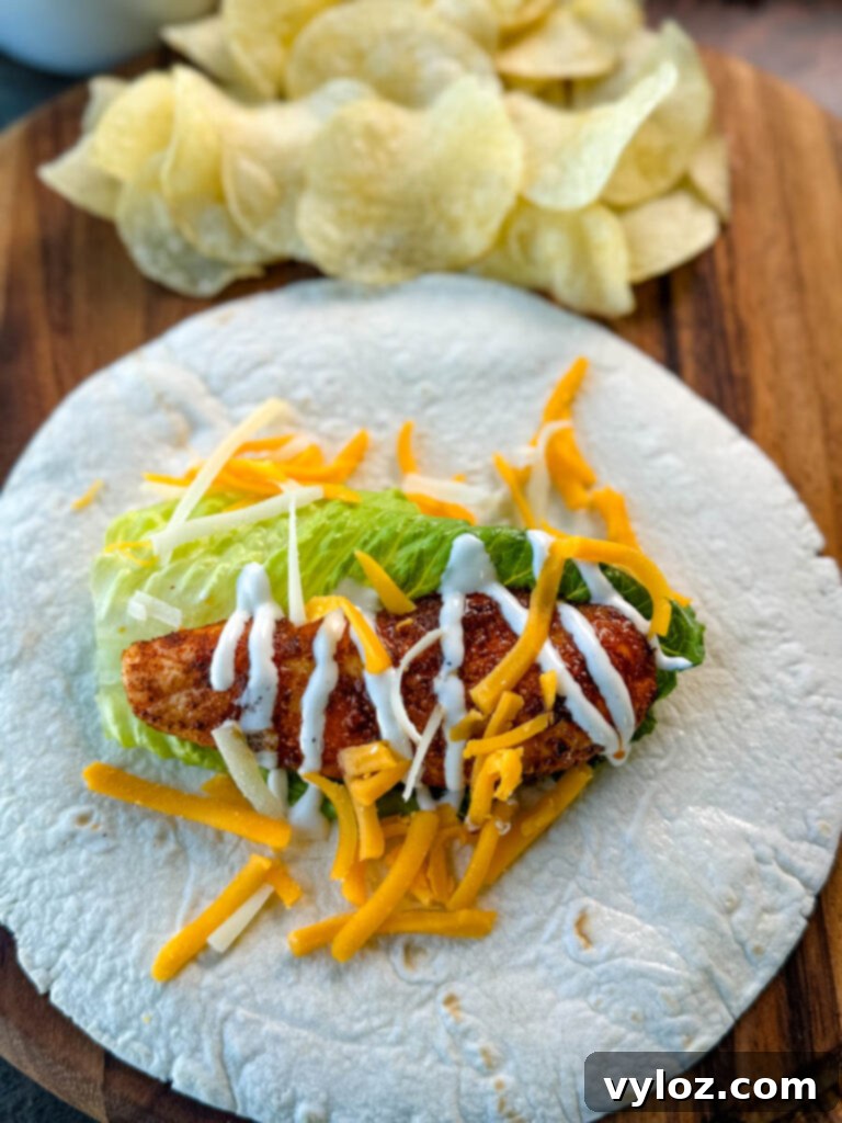 Homemade Chicken Snack Wraps 8 A plain, non-breaded chicken tender on a soft tortilla, accompanied by a dollop of ranch dressing and a sprinkle of shredded cheese.