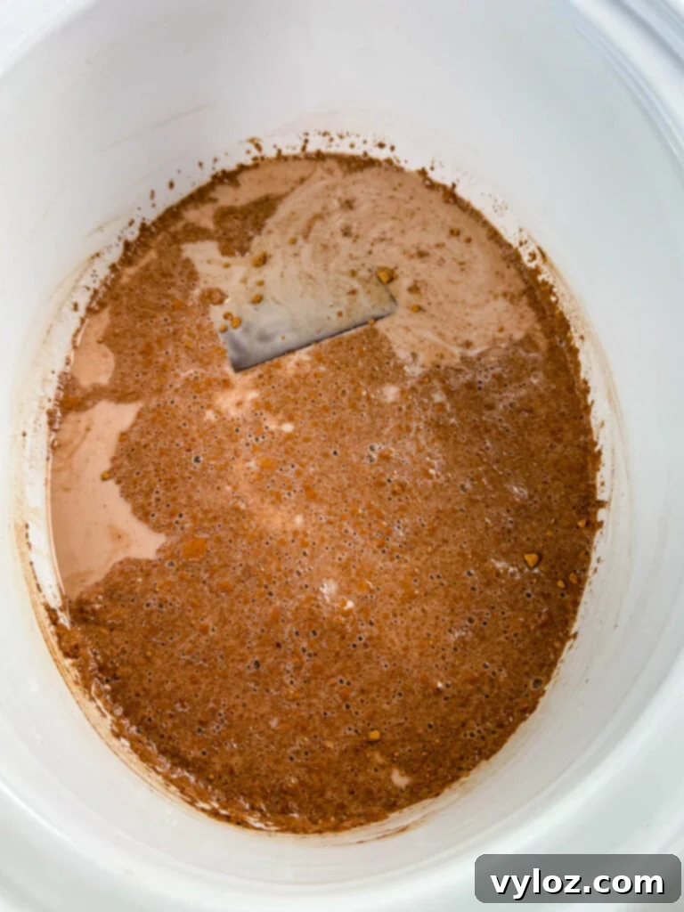 Ingredients for homemade hot chocolate, including milk, chocolate, sugar, and vanilla, being stirred in a Crockpot slow cooker before cooking.