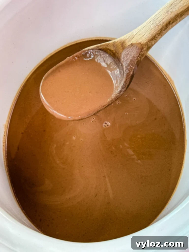 A wooden spoon stirring smooth hot chocolate in a Crockpot slow cooker, emphasizing the creamy texture.