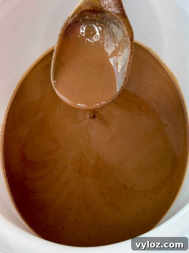 The Crockpot slow cooker, now empty, after serving delicious hot chocolate, with a wooden spoon resting inside.