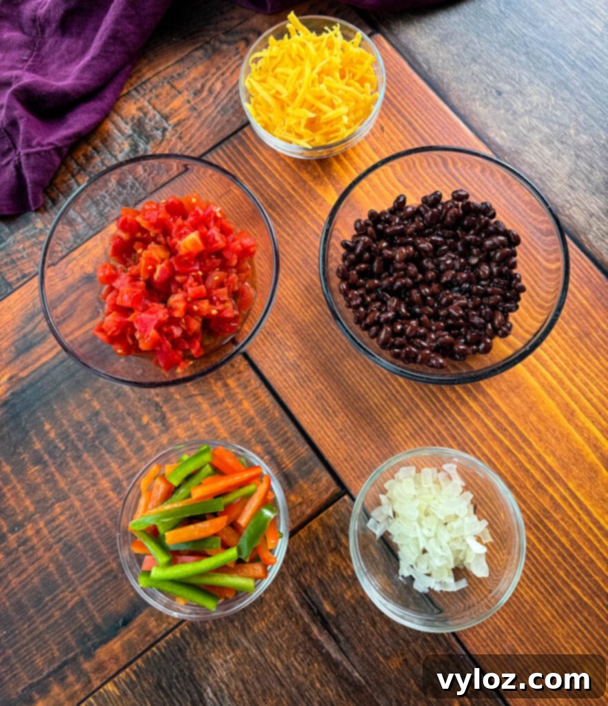 Ultimate Creamy Protein Chicken Burrito 3 Various burrito ingredients: grated cheddar cheese, diced tomatoes, black beans, sliced bell peppers, and diced onions in separate bowls