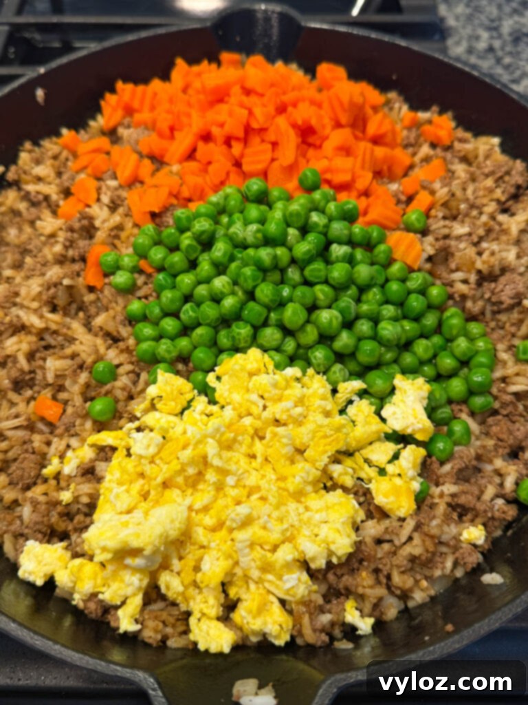 Close-up of beef fried rice in a skillet with visible eggs, peas, and carrots, being tossed.