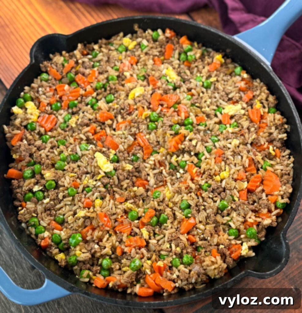 Ground beef fried rice served directly in a cast iron skillet with eggs, peas, and carrots, showcasing its rustic presentation.