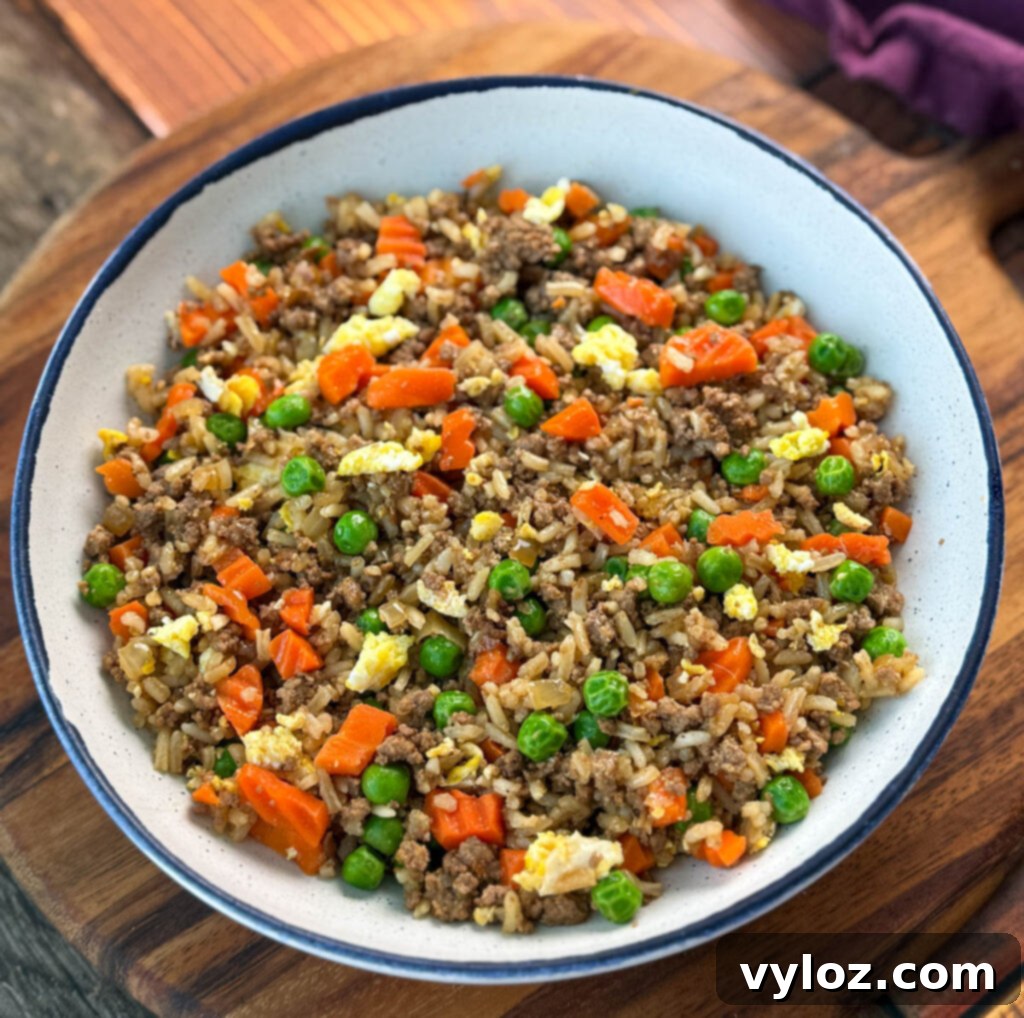 A beautifully presented bowl of ground beef fried rice, featuring eggs, peas, and carrots, ready to be served.