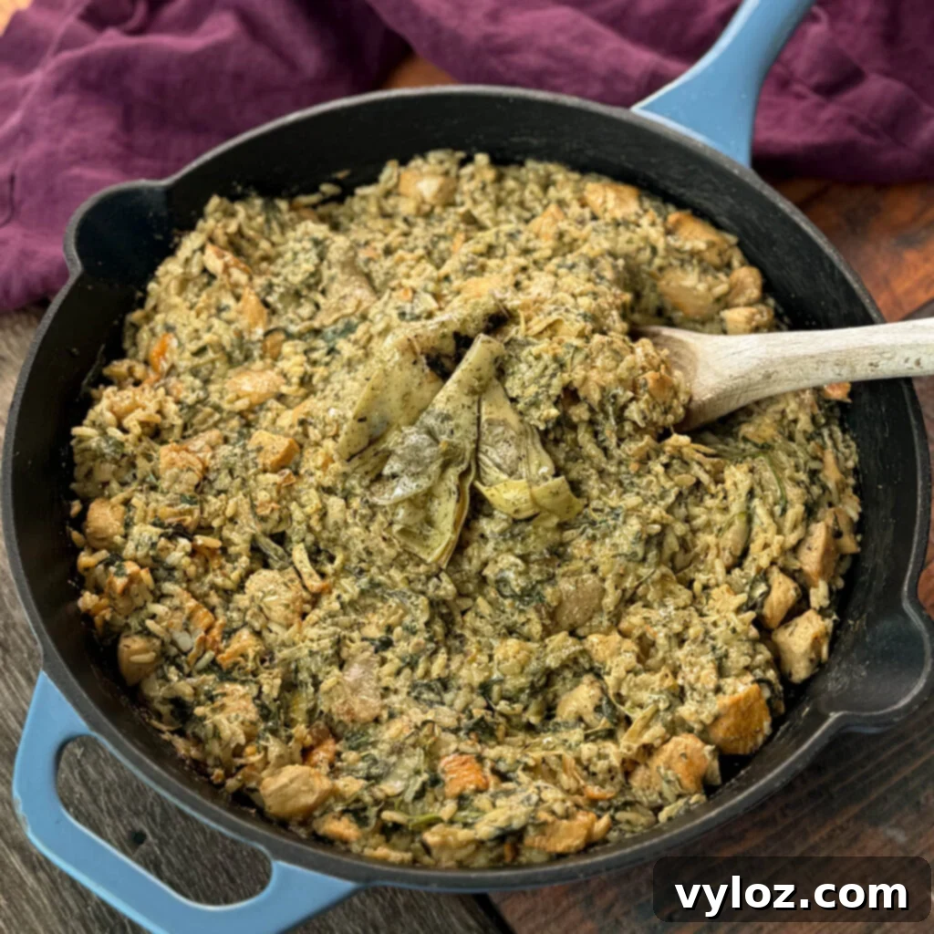 creamy spinach artichoke chicken and rice in a skillet with a wooden spoon