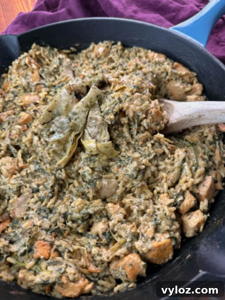 creamy spinach artichoke chicken and rice in a skillet with a wooden spoon