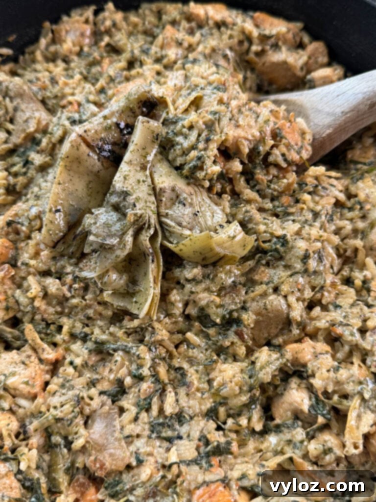 creamy spinach artichoke chicken and rice in a skillet with a wooden spoon