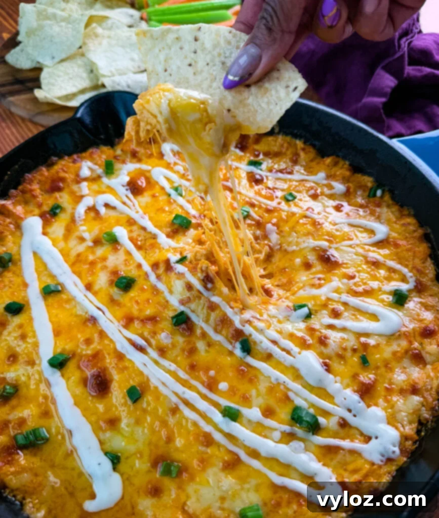 A tortilla chip lifting a scoop of gooey, melty Buffalo Chicken Dip with a perfect cheese pull.