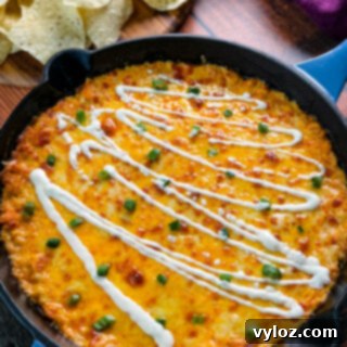 Hot and cheesy Buffalo Chicken Dip in a black cast-iron skillet, garnished with fresh green onions and a drizzle of ranch dressing, ready to be served.