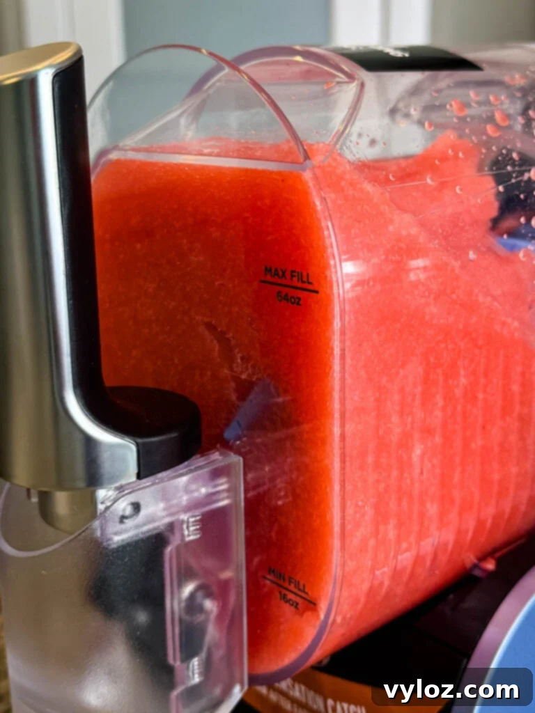 Close-up of the Ninja SLUSHi Machine’s Mixing Chamber – A transparent mixing chamber filled with bright red slush, showing the maximum and minimum fill lines on the side. The self-serve spout is visible in the foreground.